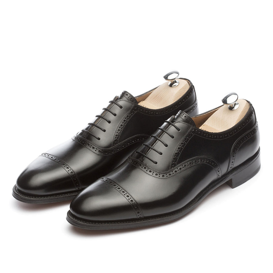 Meermin black boxcalf brogued cap-toe Oxfords, angled front pair view with shoe trees inserted, showing broguing detail and closed channel sole