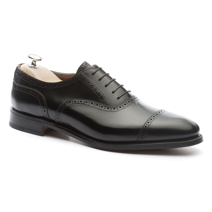 Meermin black boxcalf brogued cap-toe Oxford, angled side profile on a shoe tree, showing broguing detail and closed channel leather sole