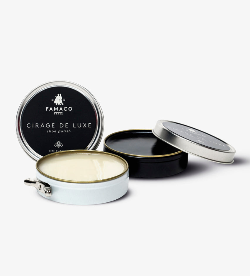 Famaco Cirage de Luxe tins open, showing cream-colored wax and black lids beside the closed branded case