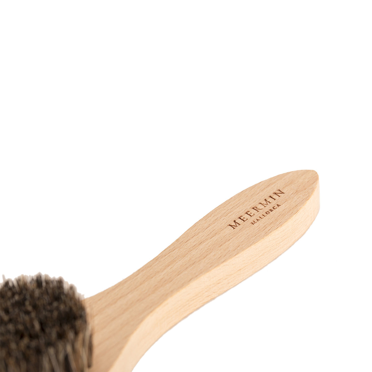Close-up of the beechwood handle's rounded end with embossed Meermin Mallorca logo, horsehair bristles blurred in background