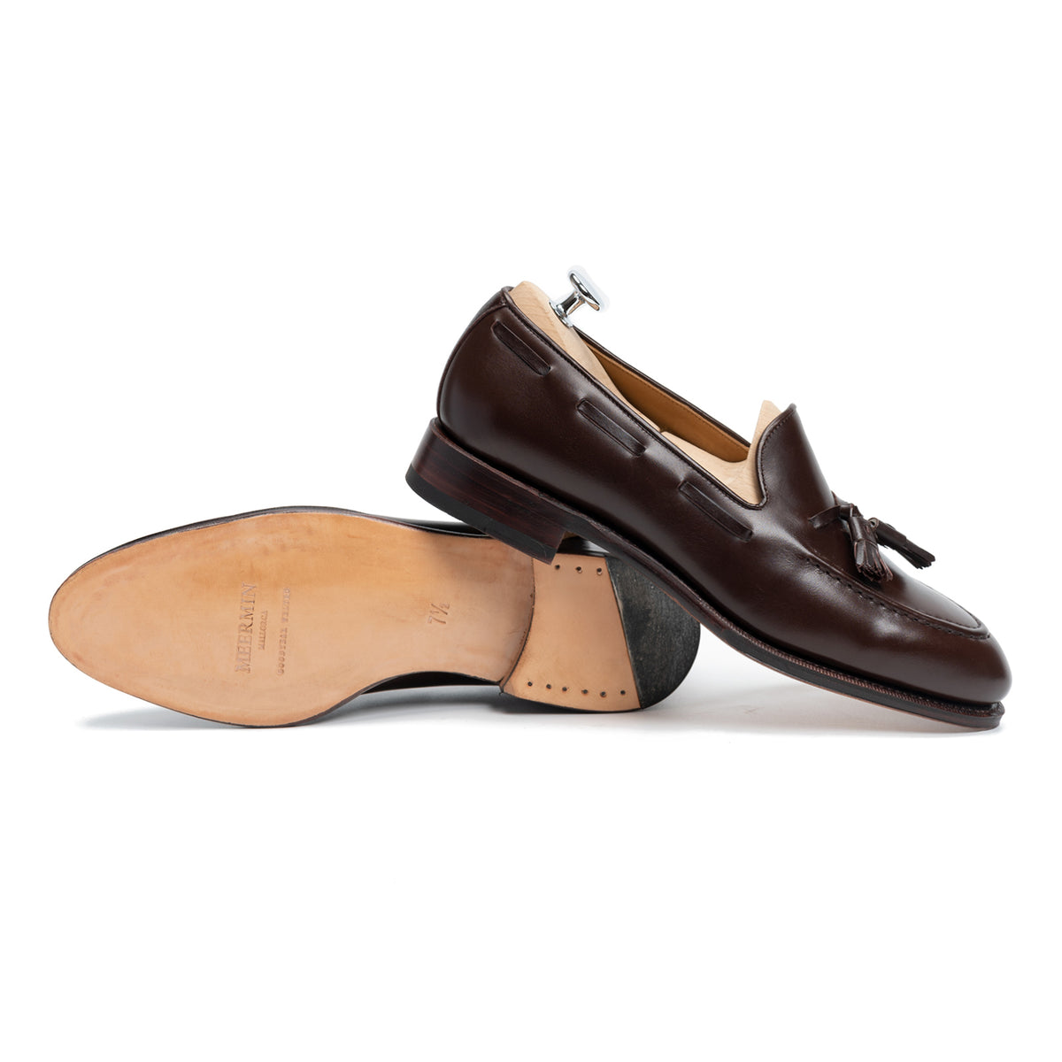 Meermin dark brown boxcalf tassel loafers, one shown sole-up revealing the leather insole and heel, the other upright on a shoe tree