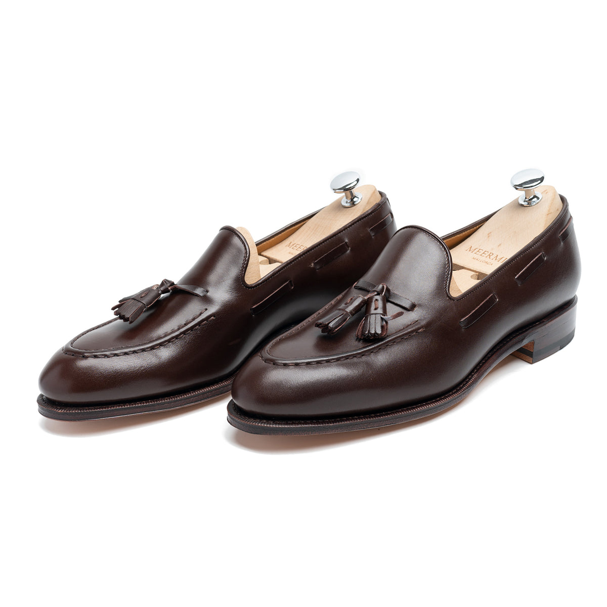Meermin dark brown boxcalf tassel loafers on shoe trees, three-quarter front view showing hand-sewn apron and tassel detail