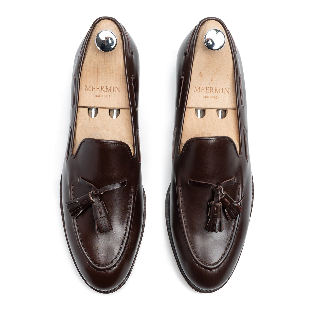 Top-down view of Meermin dark brown boxcalf tassel loafers on shoe trees, showing hand-sewn apron and tassel detail on both shoes