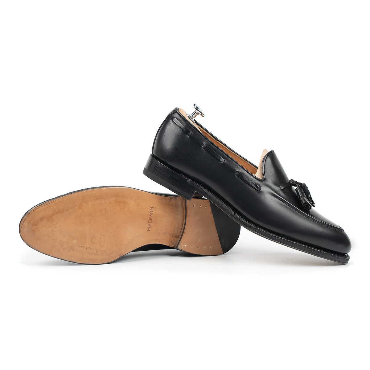 Meermin black boxcalf tassel loafers, one shoe on shoe tree, the other overturned showing the closed channel leather sole