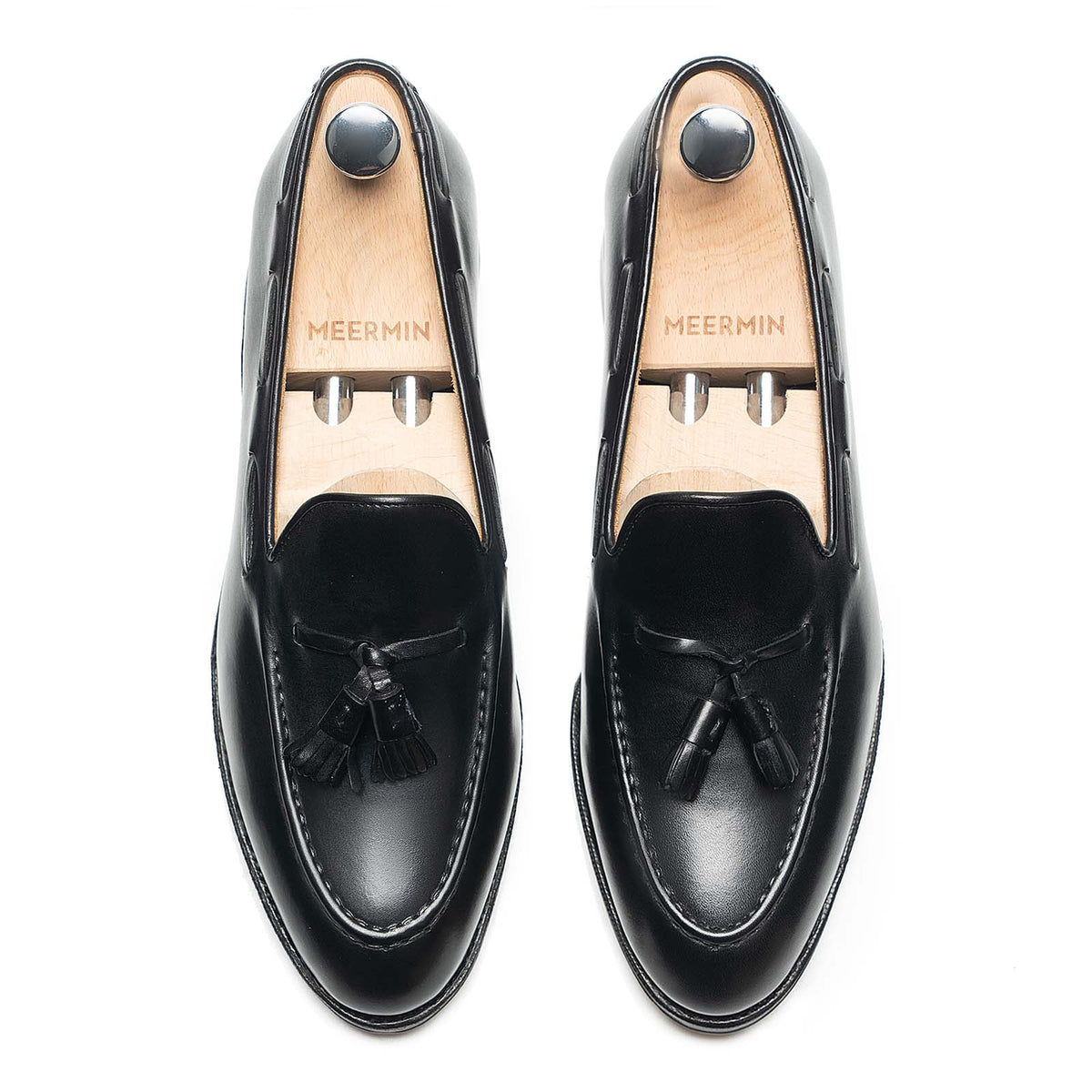Meermin black boxcalf tassel loafers, top-down view on shoe trees, showing handsewn apron and tassel detail on both shoes