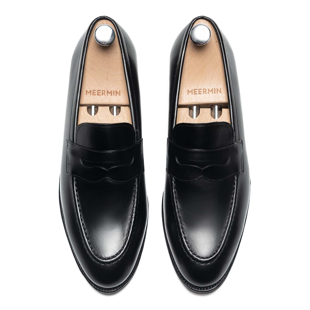 Meermin black calf penny loafers, top-down view of both shoes on wooden shoe trees, showing symmetric saddle detail