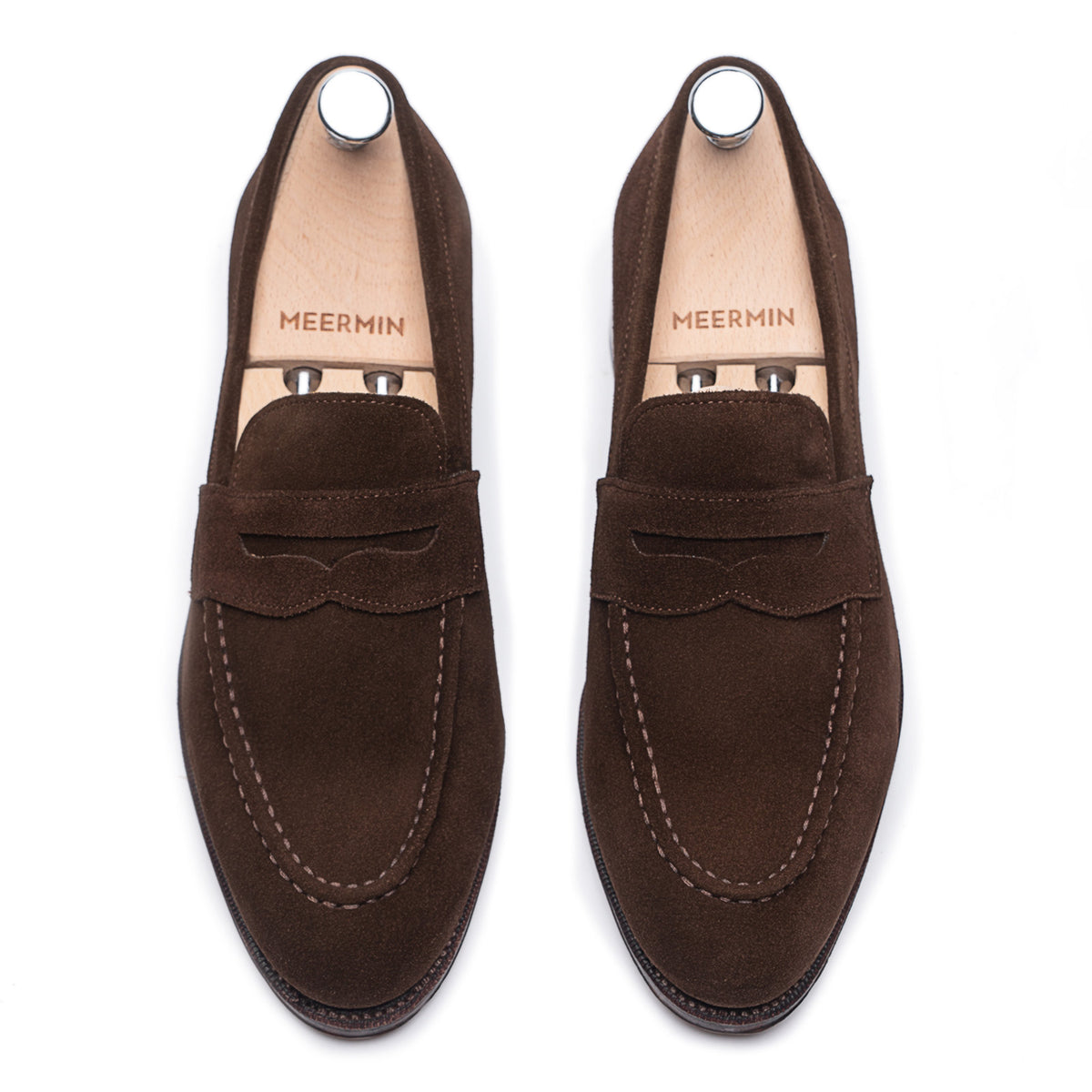 Top-down view of Meermin brown suede penny loafers on shoe trees, showing apron stitching and saddle strap detail on both shoes