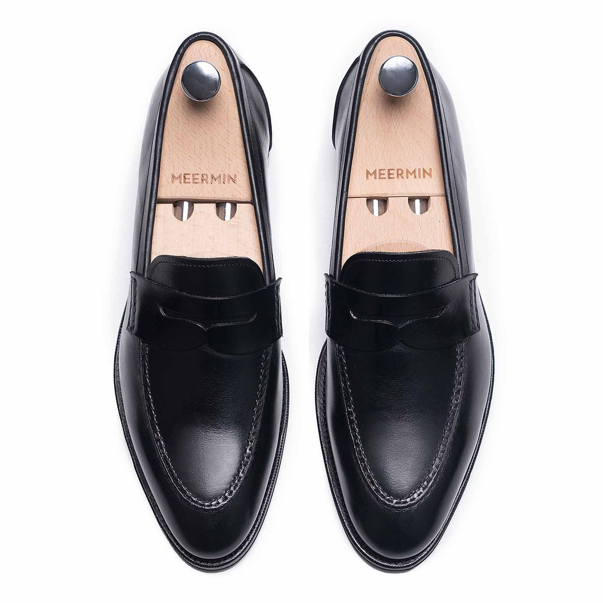 Meermin black boxcalf penny loafers, top-down view with wooden shoe trees inserted, showing apron stitch detail
