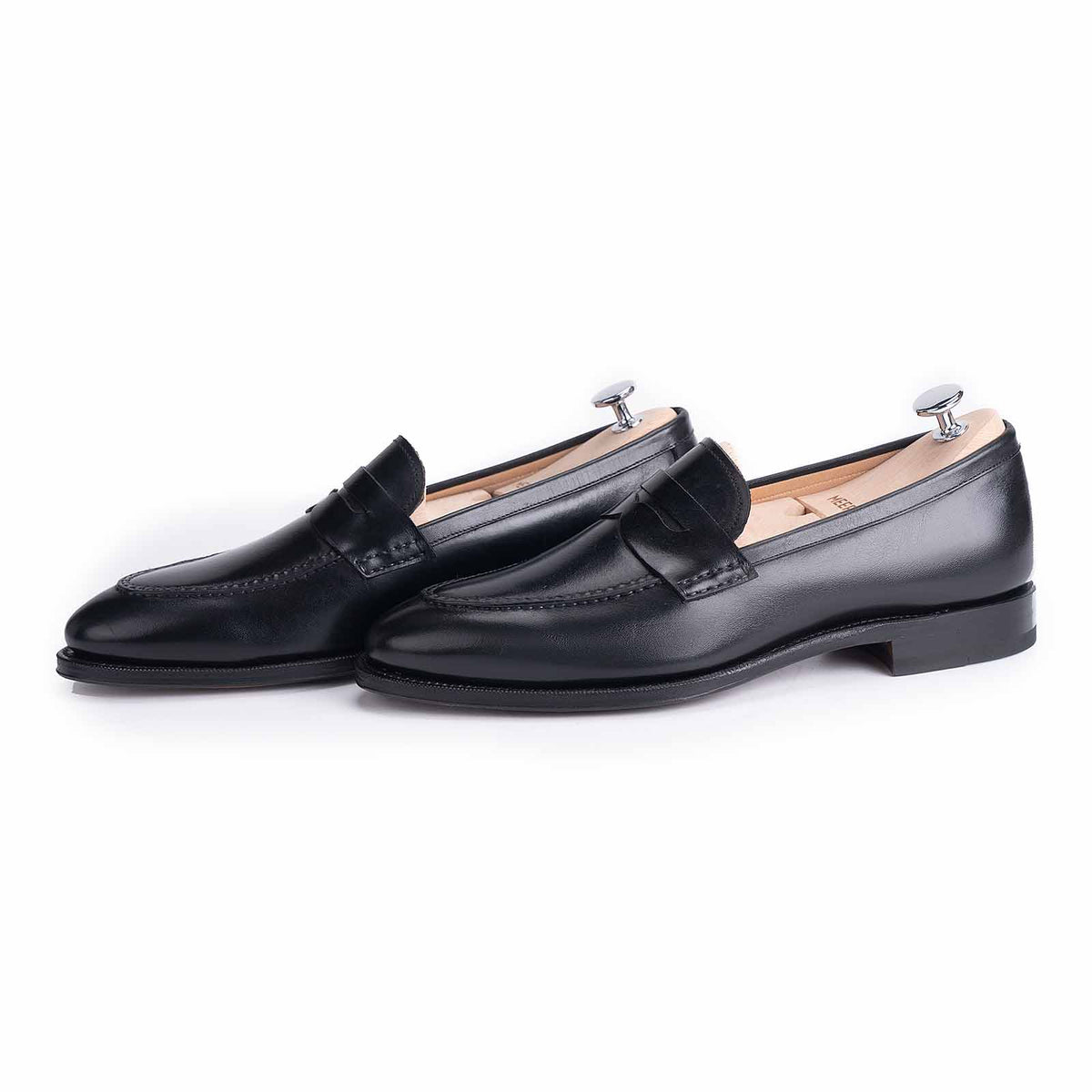 Meermin black boxcalf penny loafers, paired side-by-side with shoe trees inserted, showing apron stitch detail and closed-channel sole