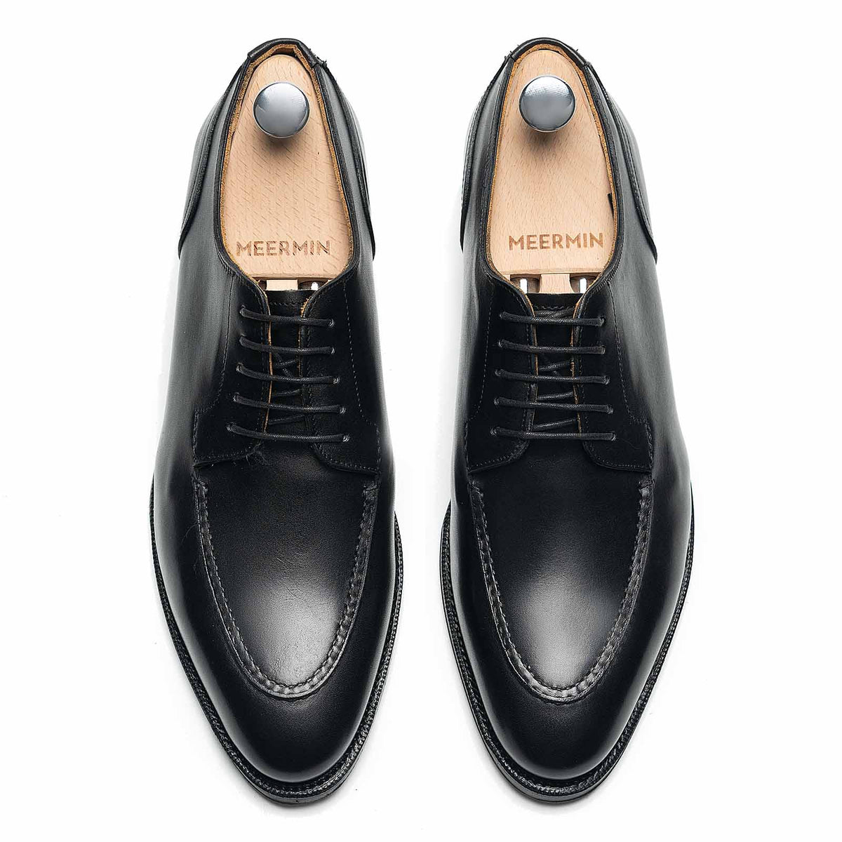 Top-down view of Meermin black boxcalf Norwegian derby pair on shoe trees, showing pie-crust apron stitching and lace-up vamp