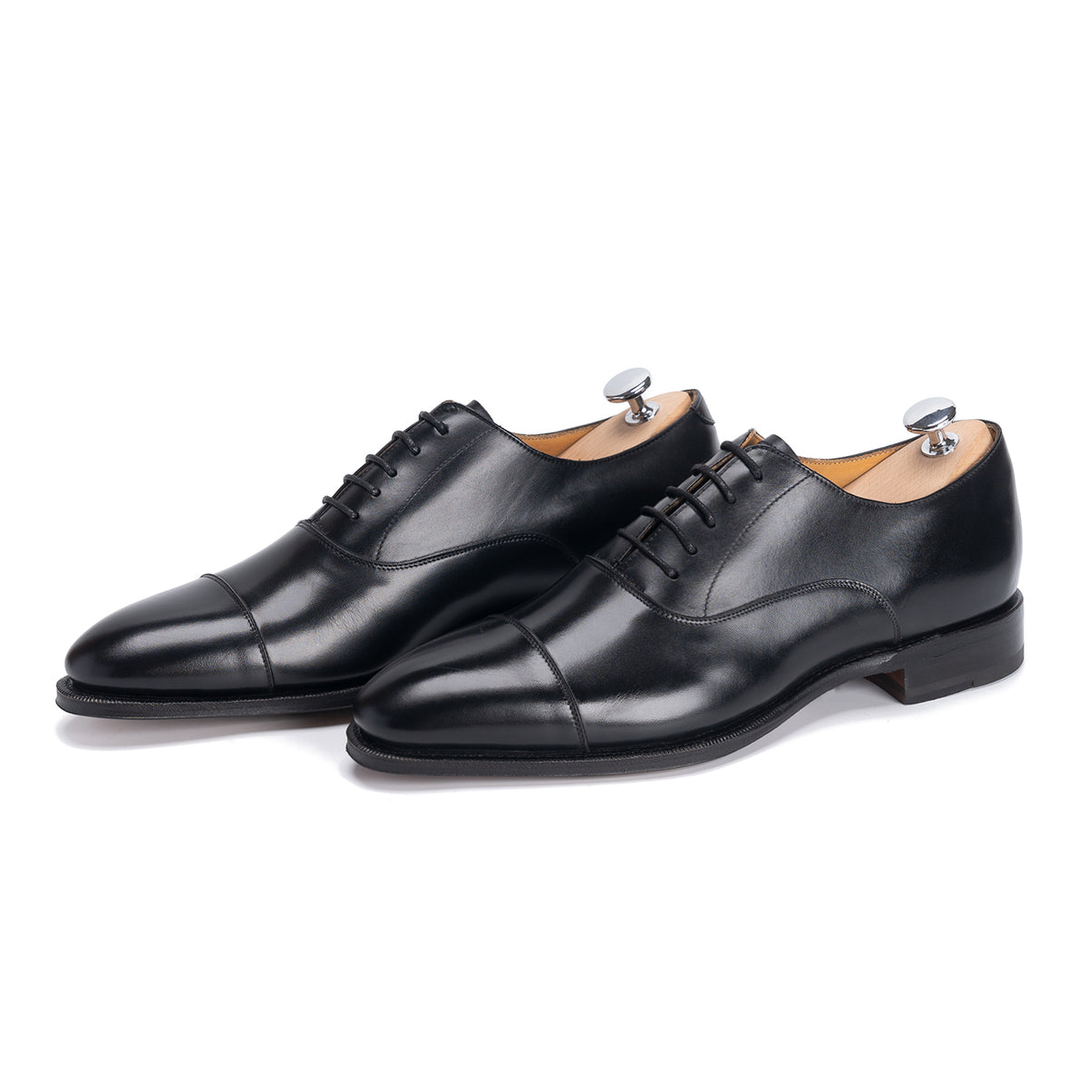Meermin black calfskin cap-toe Oxfords, three-quarter side view with shoe trees inserted, showing lace panels and stacked heels