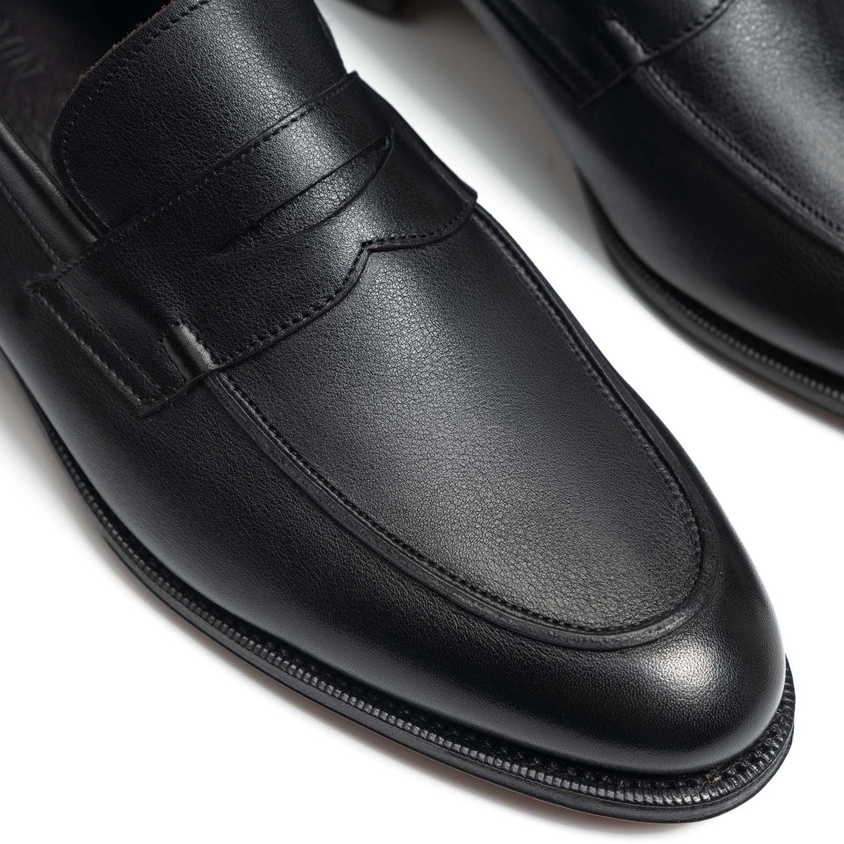 Meermin black softcalf penny loafers, close-up on the vamp strap and apron seam showing the unlined leather's soft grain texture