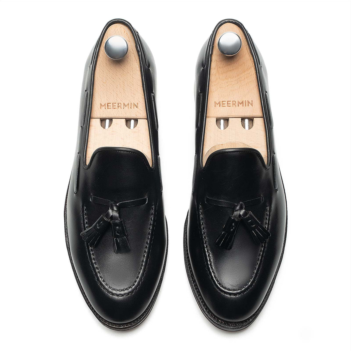 Meermin black calf tassel loafers, top-down view on shoe trees, showing hand-sewn apron and tasseled front detail
