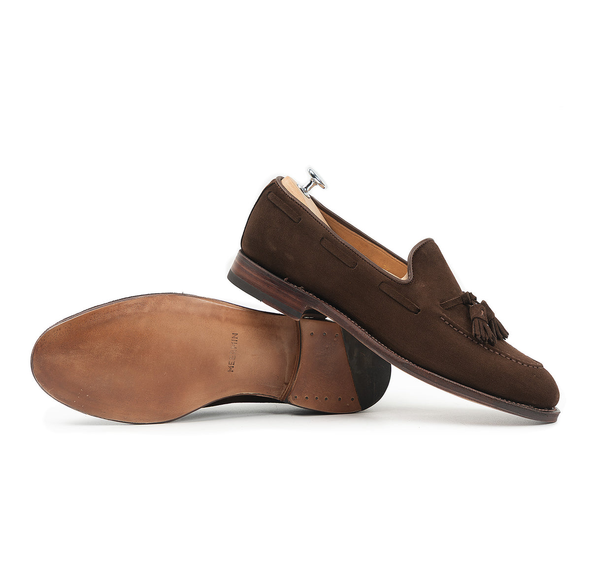 Meermin brown suede tassel loafers, one shown sole-up revealing leather sole and heel stack, the other resting on a shoe tree