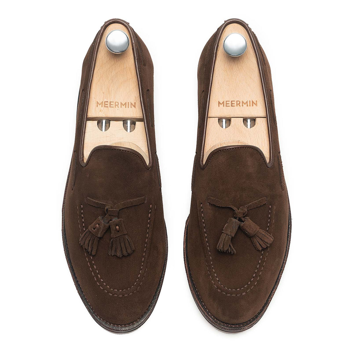 Meermin brown suede tassel loafers, top-down view on shoe trees, showing hand-closed tassels and apron stitching