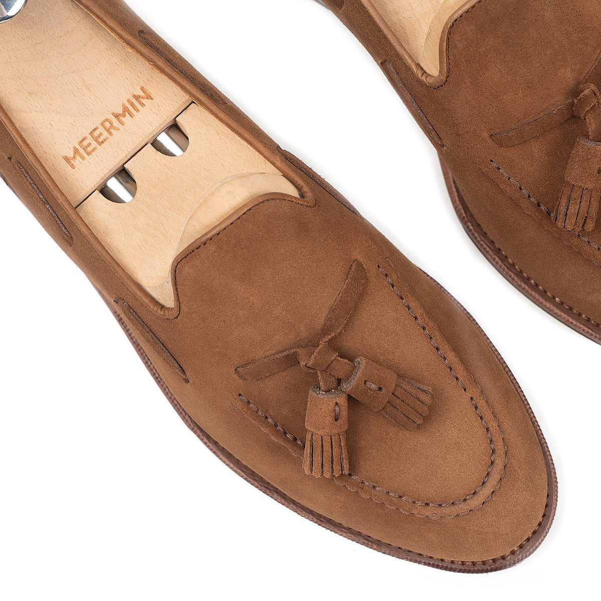 Close-up of Meermin snuff suede tassel loafers on shoe trees, showing hand-sewn apron stitching and hand-closed tassel detail