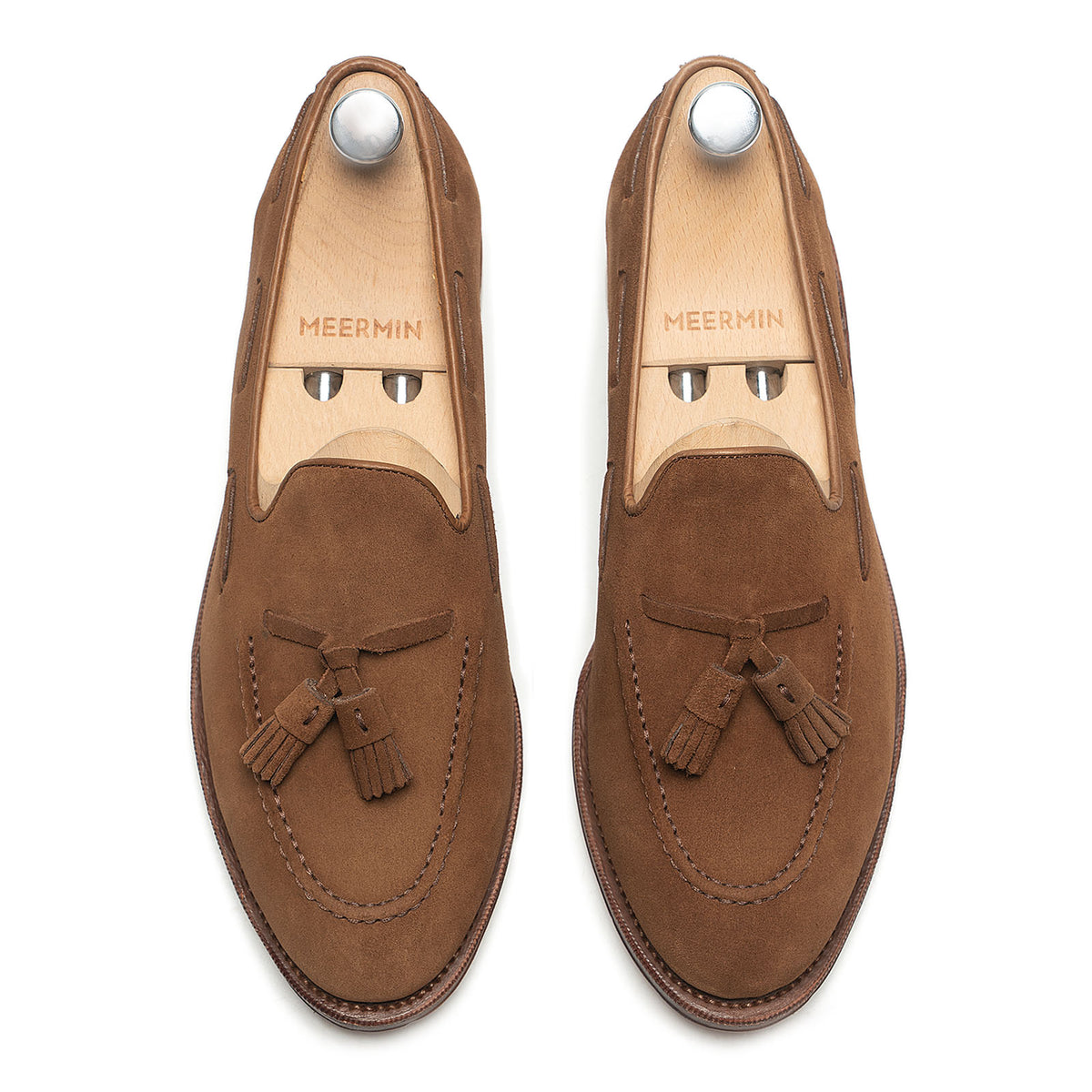 Meermin snuff suede tassel loafers, top-down view on shoe trees, showing hand-closed tassels and apron stitching detail