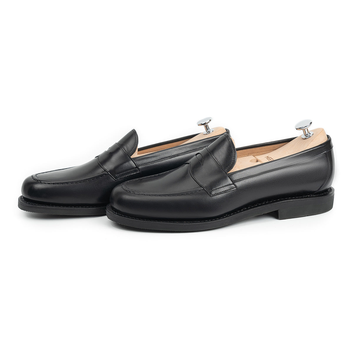 Meermin black calf penny loafers, side-by-side three-quarter view with shoe trees inserted, showing studded rubber sole and apron stitching