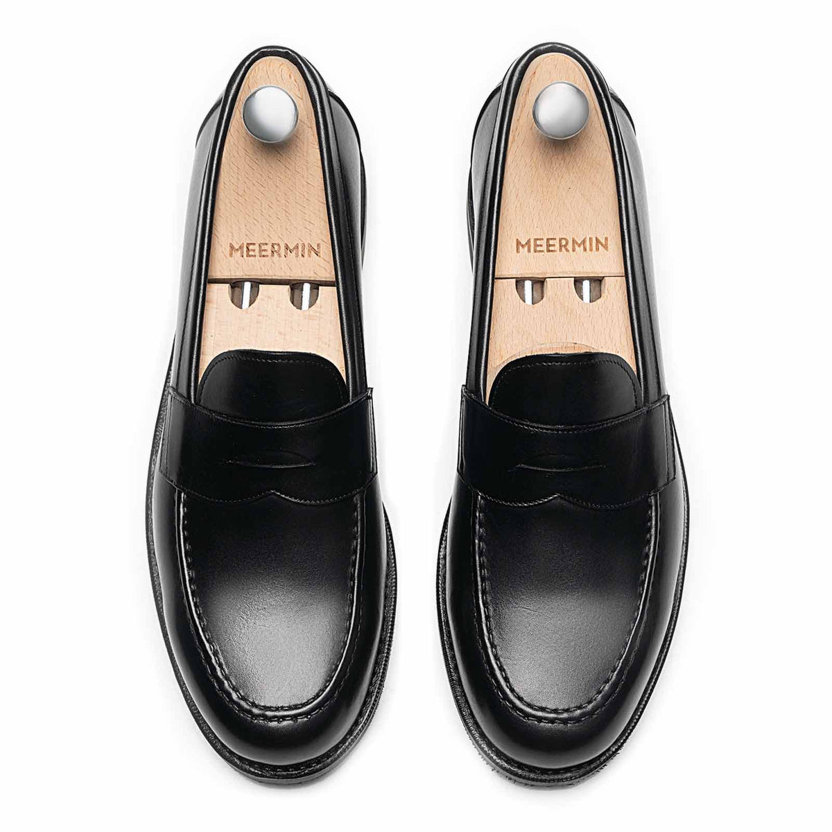 Meermin black calf penny loafers, top-down view on shoe trees, showing apron stitching and studded rubber soles