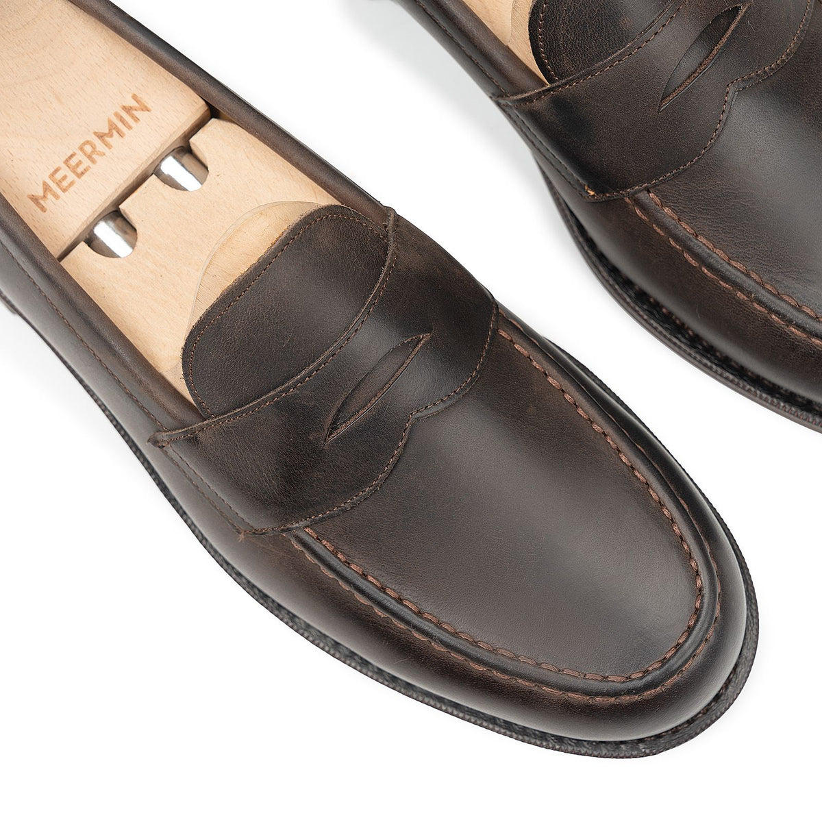 Meermin brown waxy calf penny loafers on wooden shoe trees, close-up top view highlighting apron stitching and saddle strap detail