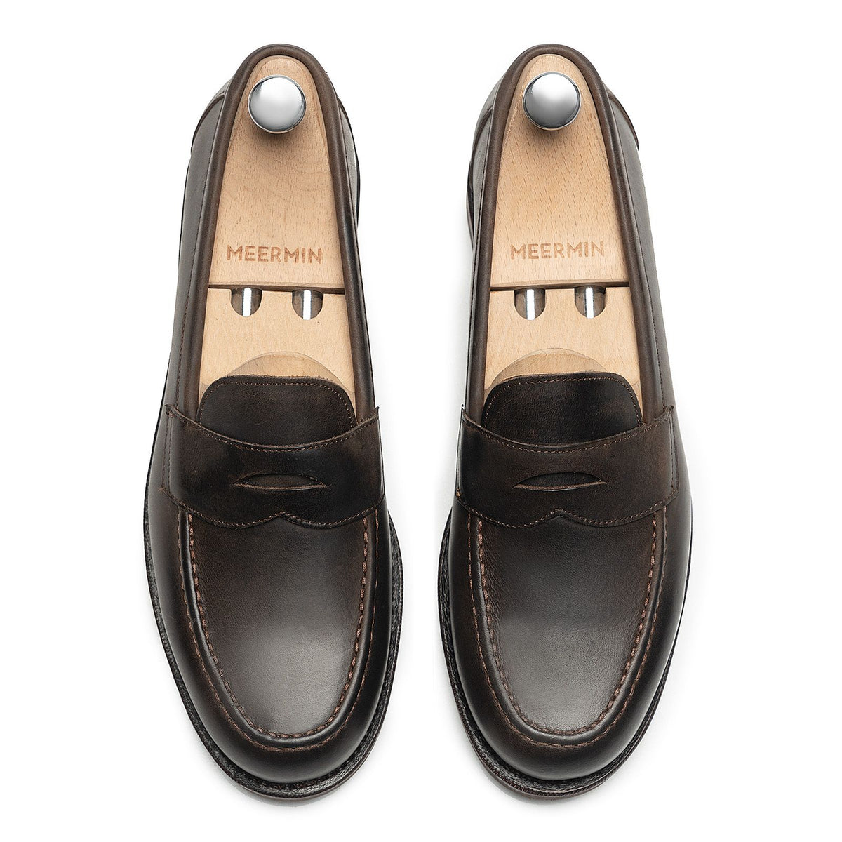 Meermin brown waxy calf penny loafers, top-down view on shoe trees, showing apron stitching and moc-toe seam detail