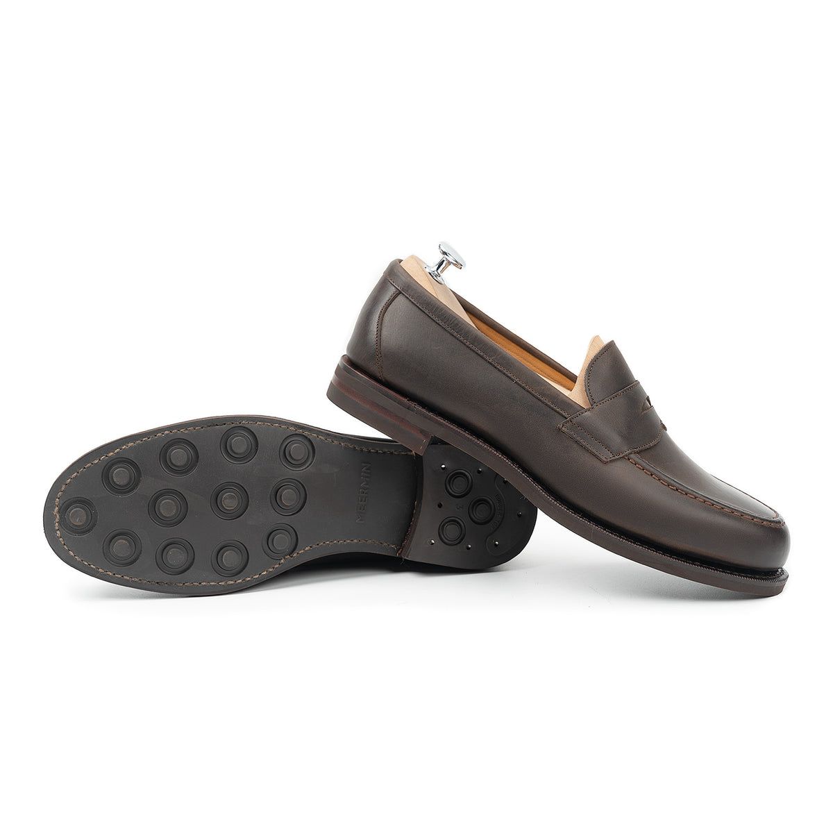 Meermin brown waxy calf penny loafers, one shoe on shoe tree, the other tipped over showing studded rubber outsole