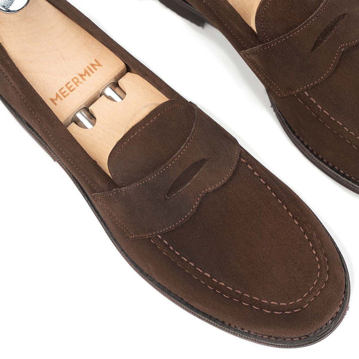 Close-up of Meermin brown suede penny loafers with wooden shoe trees inserted, showing apron stitching and toe shape detail