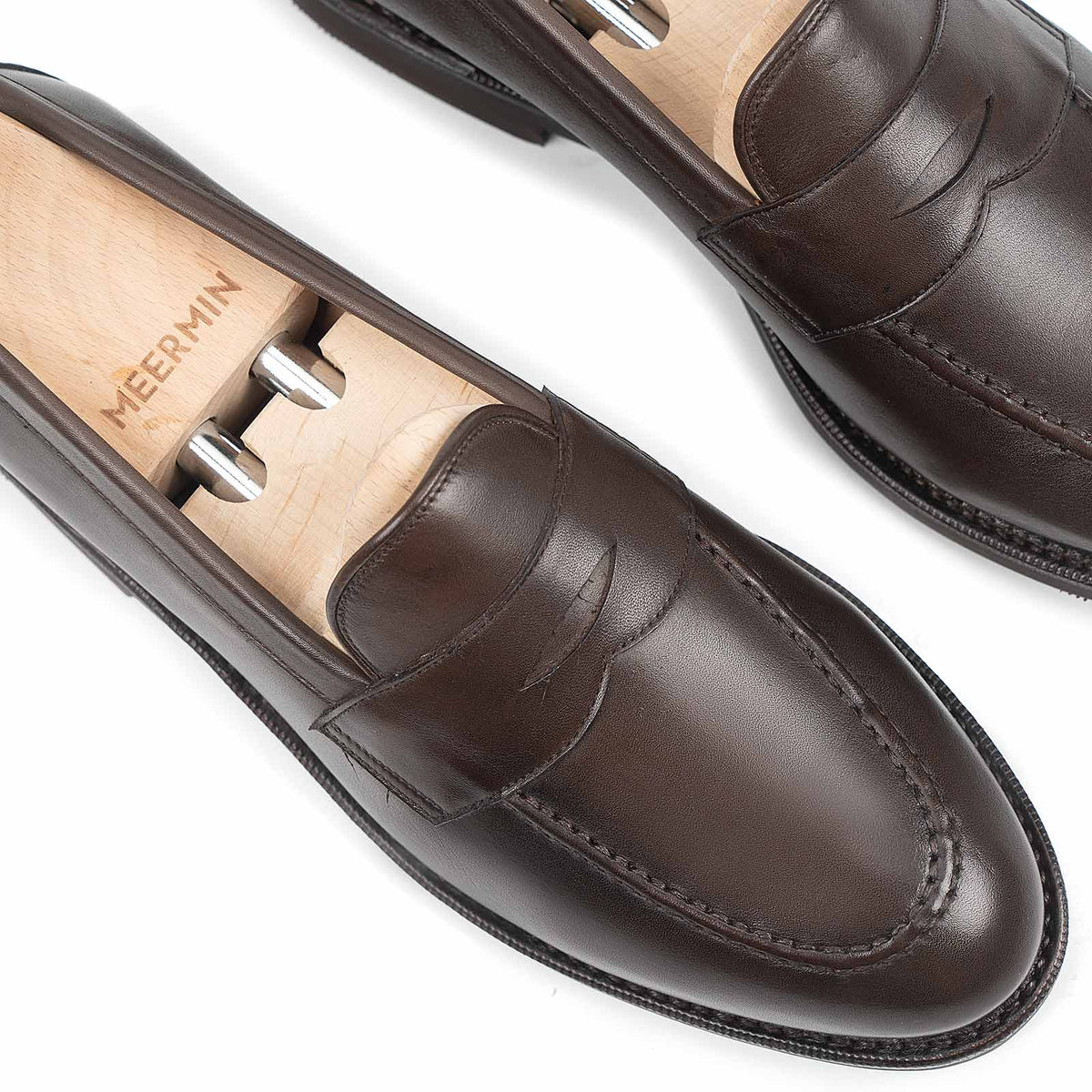Close-up of Meermin brown silkcalf penny loafers with handsewn aprons, shown on wooden shoe trees highlighting the moc-toe stitching