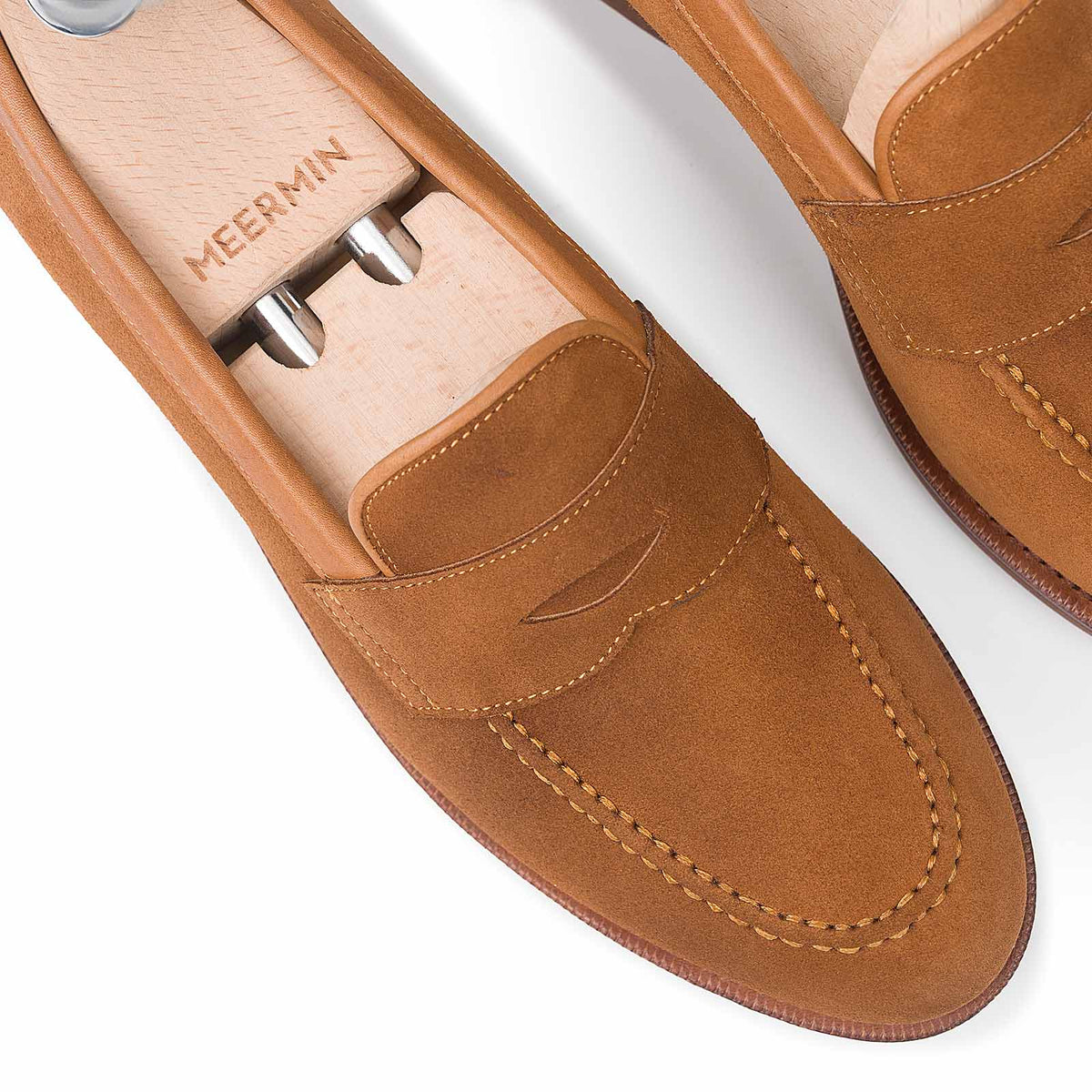 Close-up top view of Meermin copper Alicante suede penny loafers on wooden shoe trees, showing stitched apron and strap detail