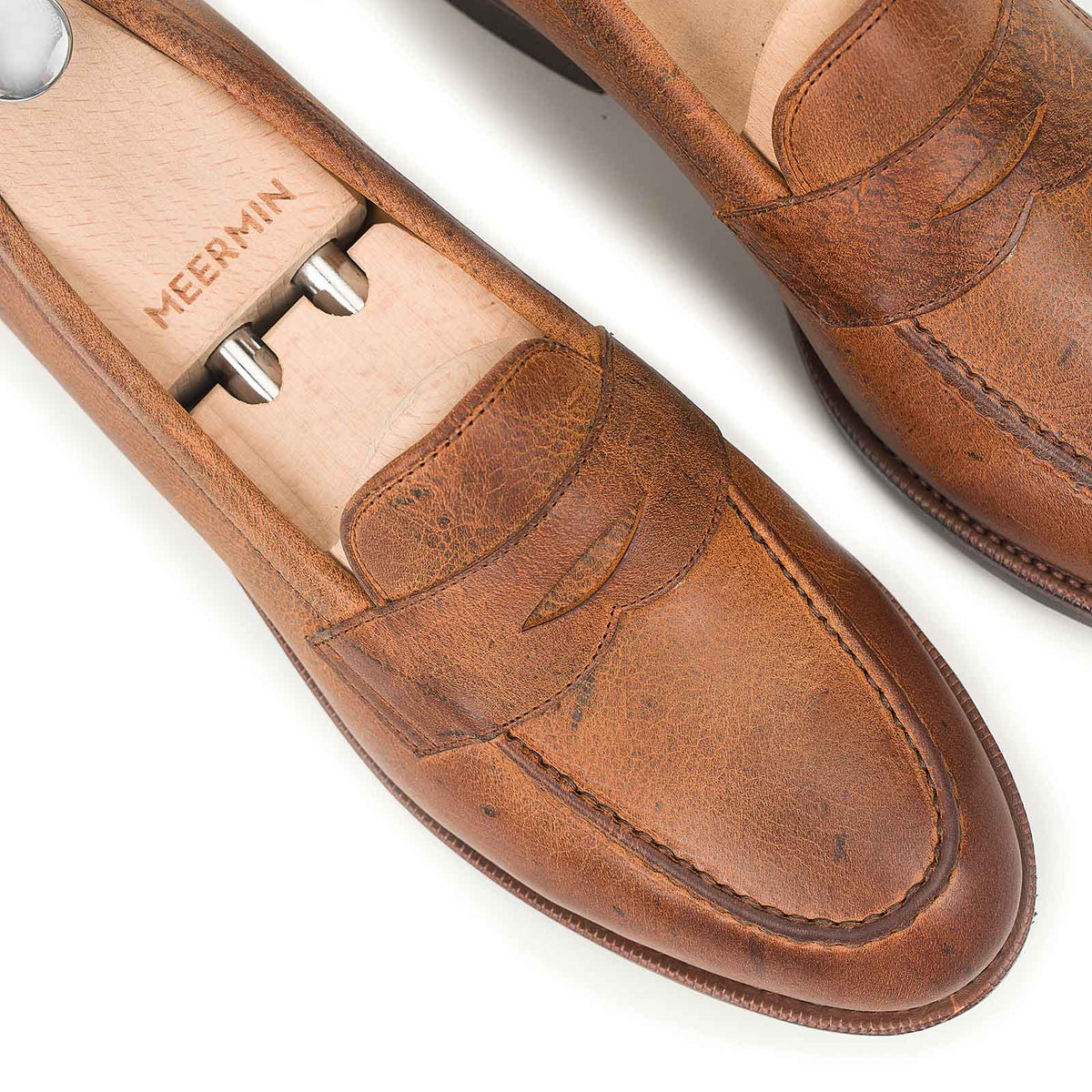 Close-up of Meermin Autumn Spice waxy Kudu penny loafers on shoe trees, showing textured grain and saddle stitching detail