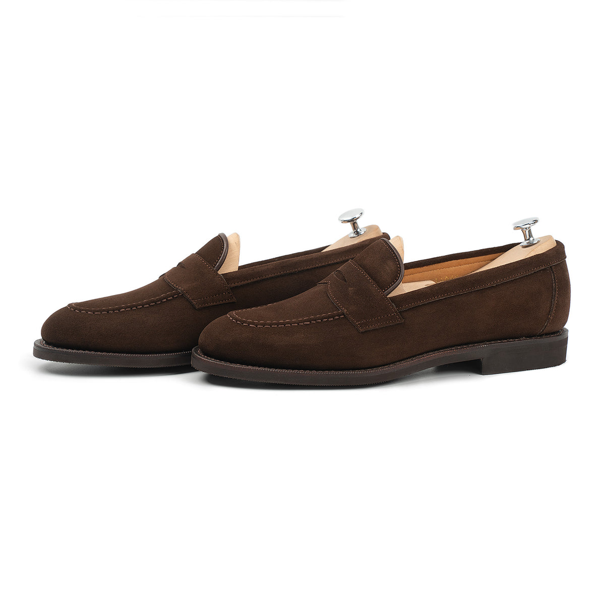 Meermin brown suede penny loafers, three-quarter side view on shoe trees, showing apron stitching and diamond rubber sole edge
