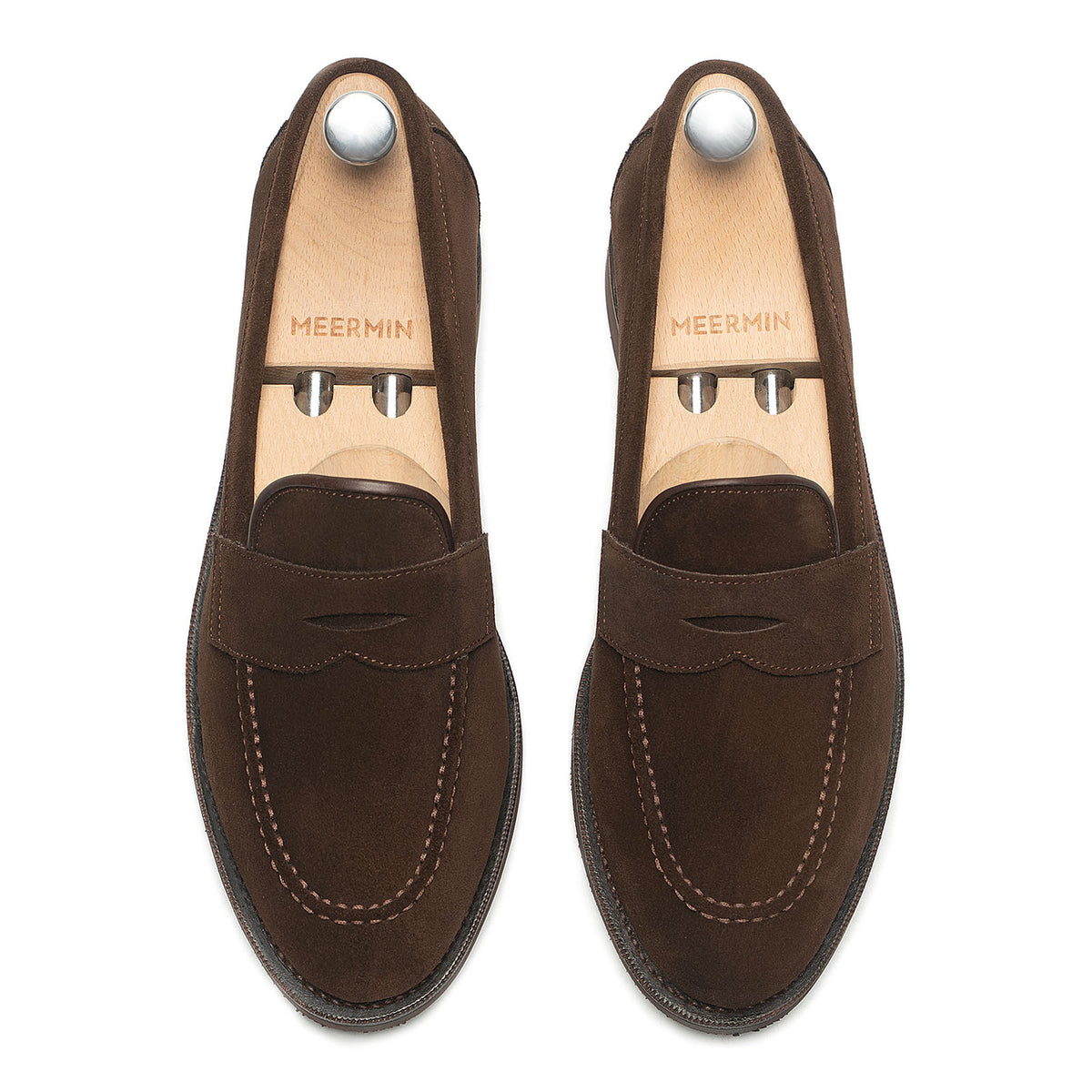 Top-down view of Meermin brown suede penny loafers on shoe trees, showing moc-toe stitching and saddle strap detail on both shoes