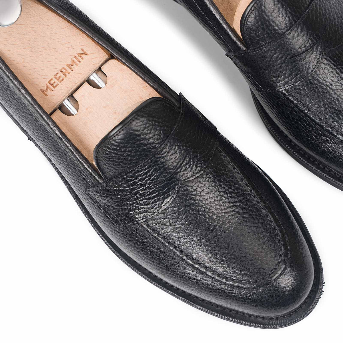 Close-up of Meermin black Inca grain leather penny loafers on shoe trees, showing handsewn apron detail and toe shape