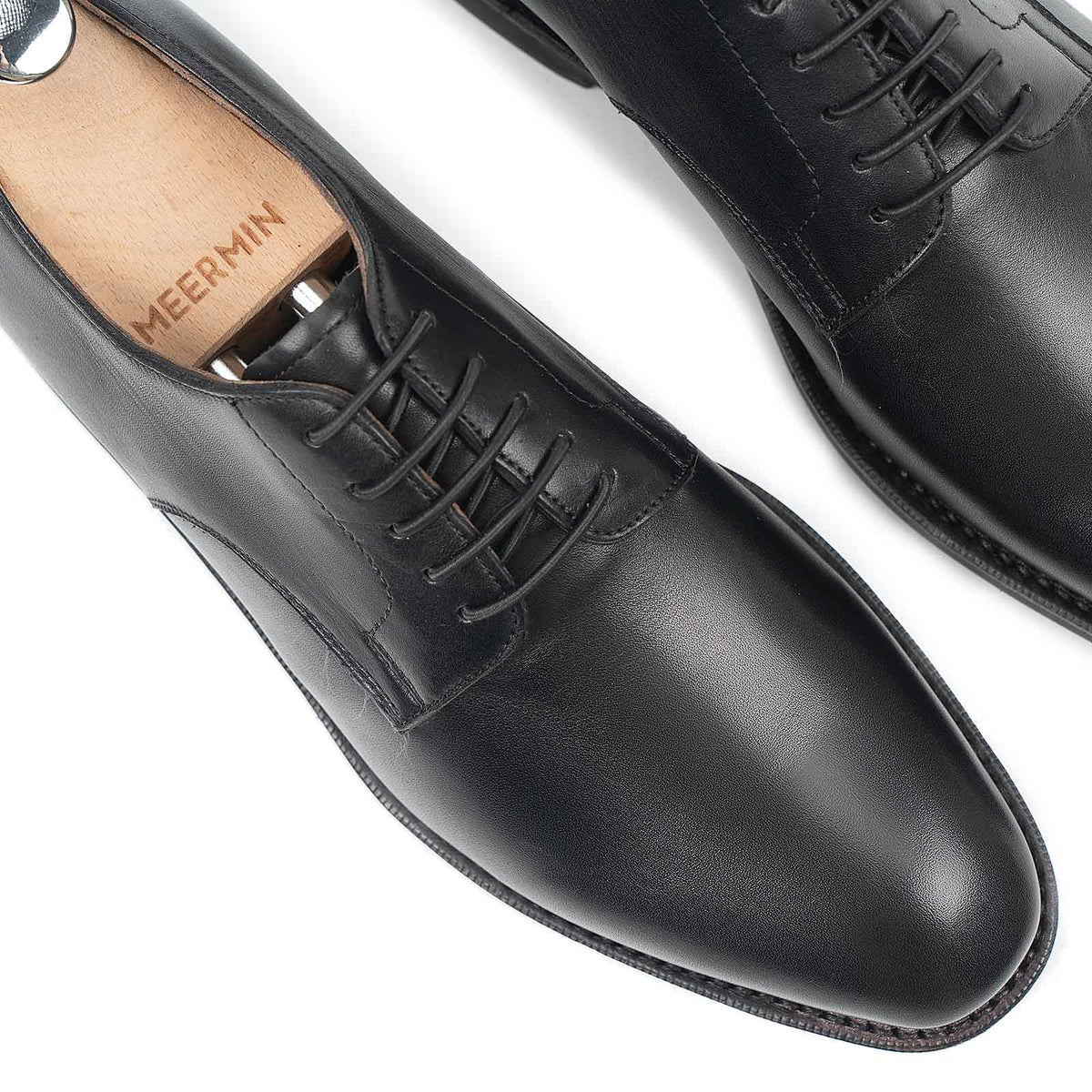 Close-up top view of Meermin black silkcalf plain toe bluchers, showing lace panels and toe caps with wooden shoe trees inserted