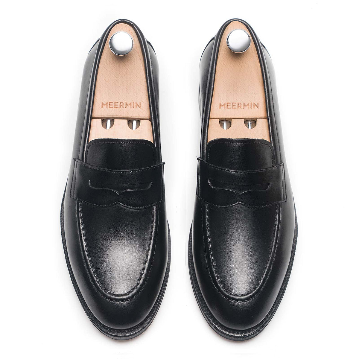 Meermin black boxcalf penny loafers, top-down view on shoe trees, showing saddle strap and apron toe detail