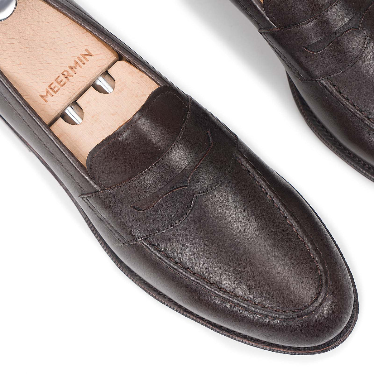 Close-up top view of Meermin espresso antique calf penny loafers on wooden shoe trees, showing saddle strap stitching detail