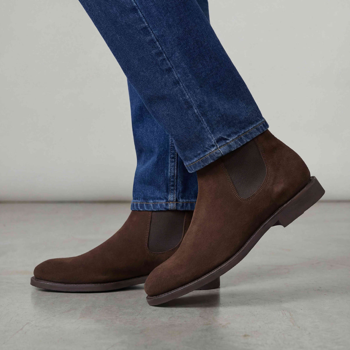Meermin brown suede Chelsea boots worn with jeans, side profile shot showing elastic gusset and diamond rubber sole mid-stride