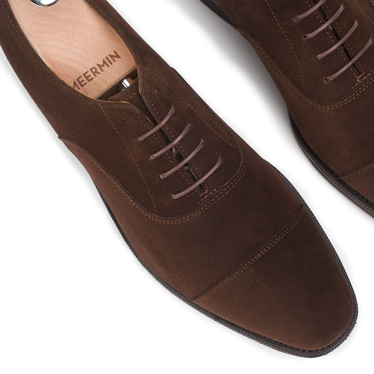 Close-up top view of Meermin brown suede cap-toe Oxfords with shoe trees, showing lace eyelets and stitched toe cap detail