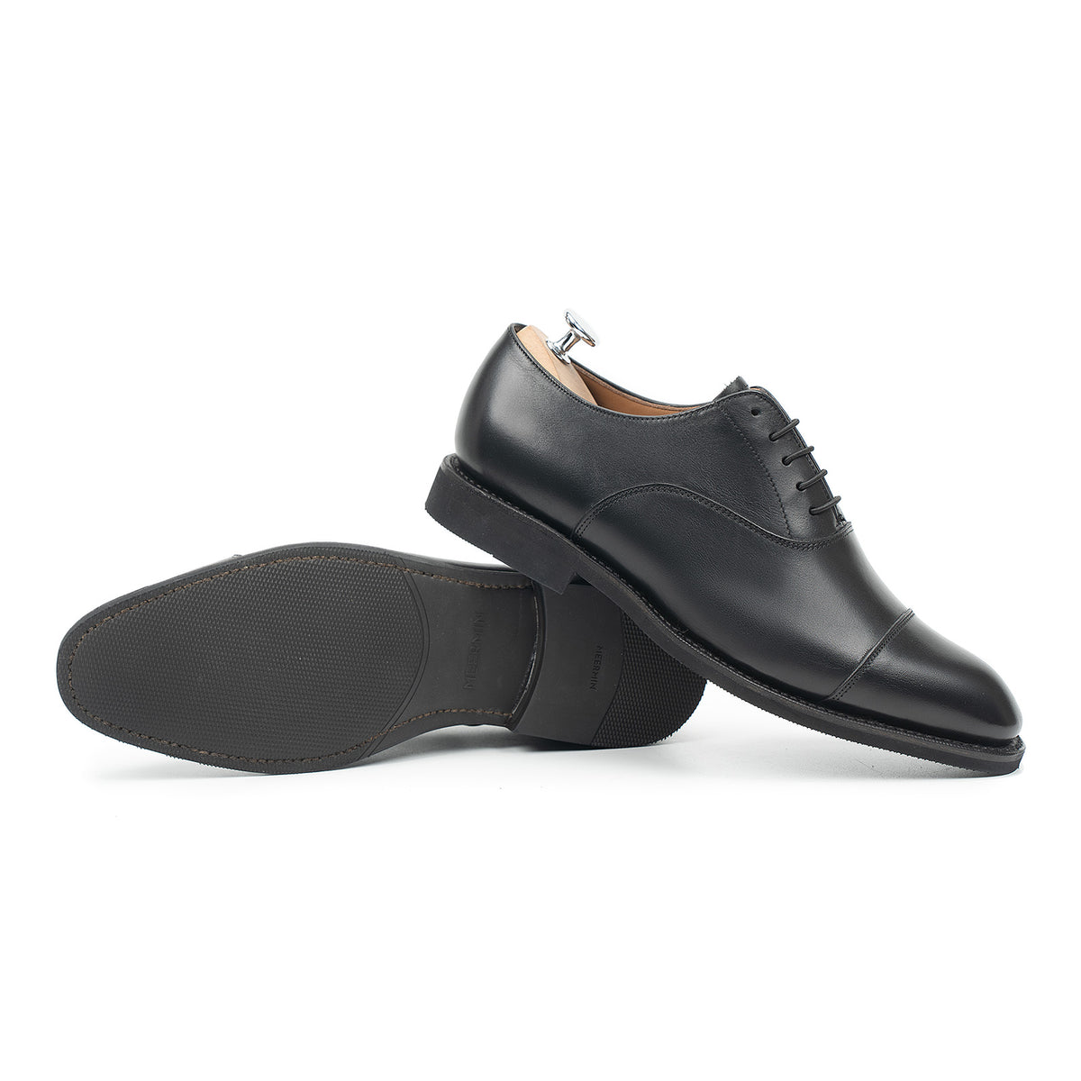 Meermin black silkcalf cap-toe Oxfords, one shoe on its side showing the diamond latex rubber sole, the other upright with shoe tree