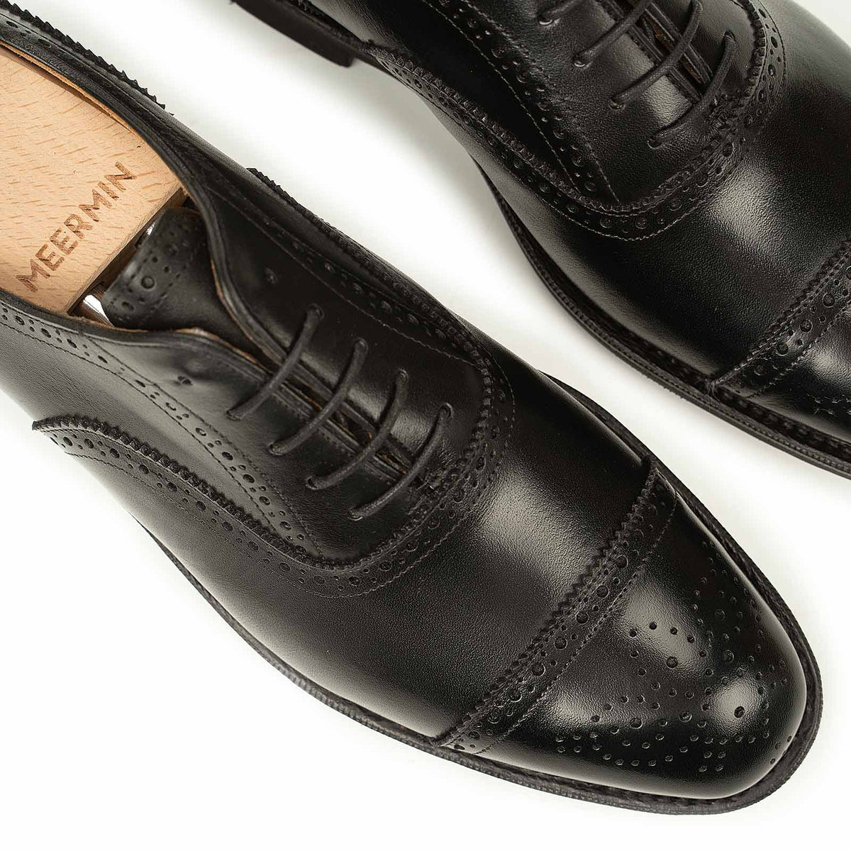 Close-up top view of Meermin black boxcalf full brogue Oxfords, showing perforated cap-toe detailing and lacing with wooden shoe trees inserted