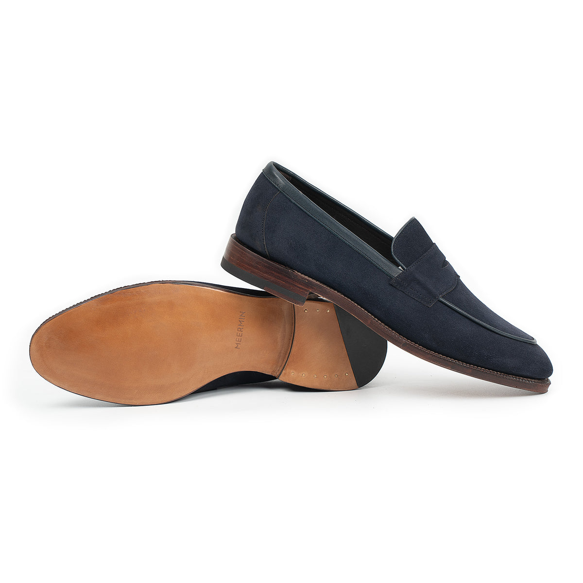 Meermin navy suede penny loafer pair, one shoe resting sole-up against the other showing tan leather insole and heel stack