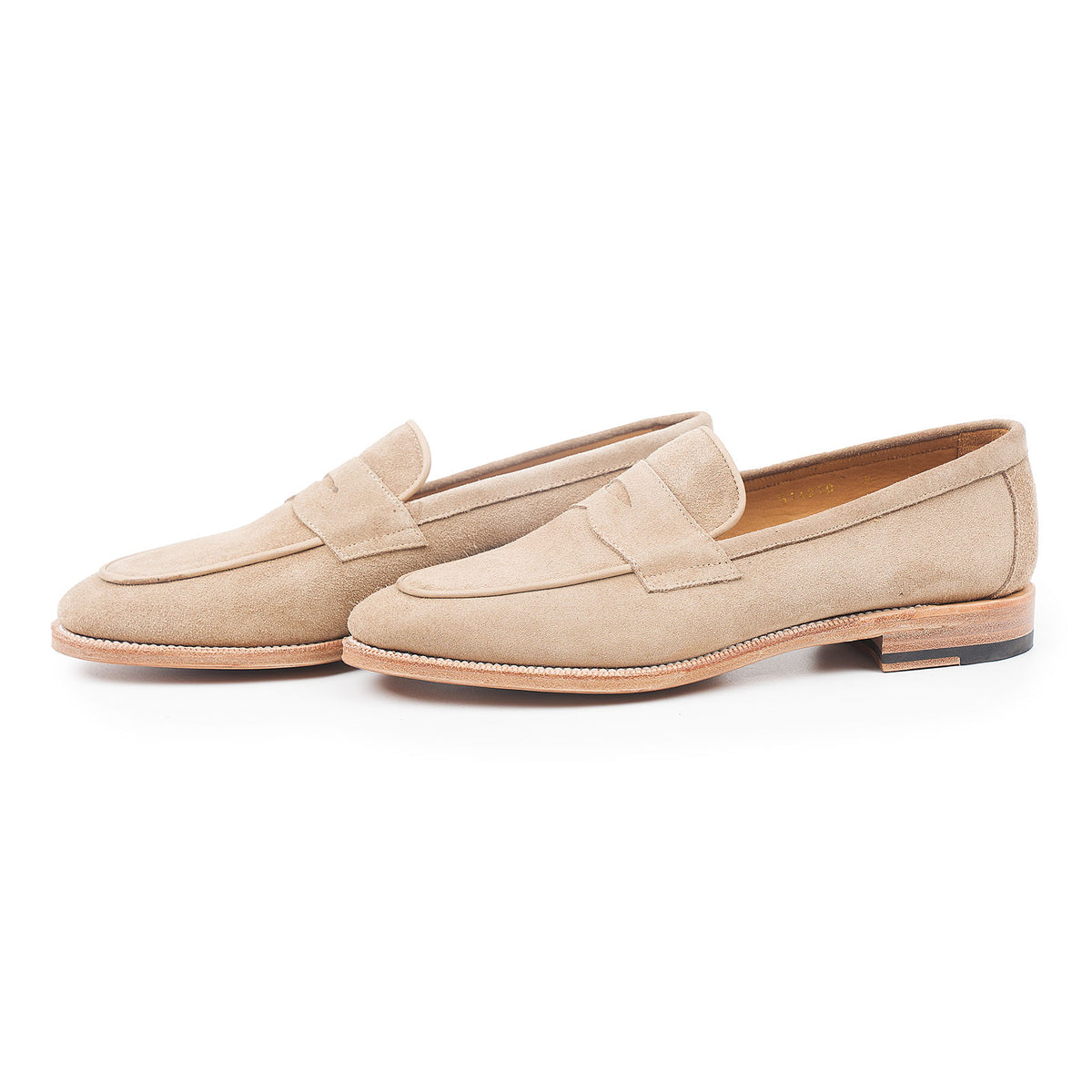 Meermin taupe suede penny loafers, three-quarter side view showing both shoes with piping apron detail and leather sole