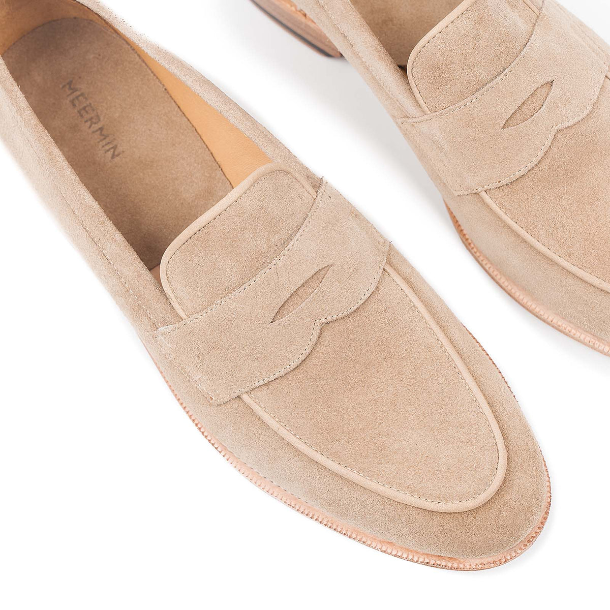 Close-up top view of Meermin taupe suede penny loafers, showing piping apron detail and strap cutouts on both shoes