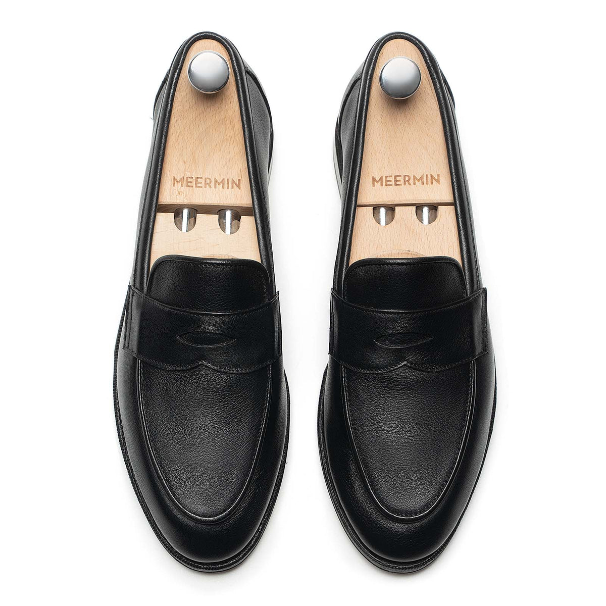 Meermin black softcalf penny loafers, top-down view on shoe trees, showing smooth apron piping and rounded toe silhouette