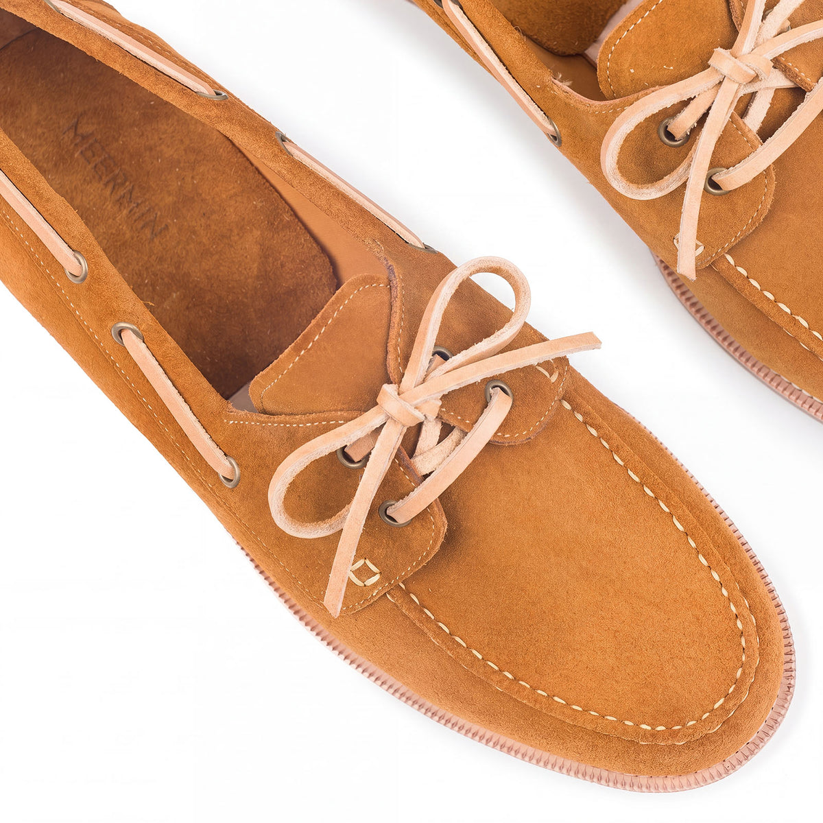 Close-up of Meermin tobacco suede deck shoes, showing vegetable-tanned leather laces tied in a bow and brass eyelets