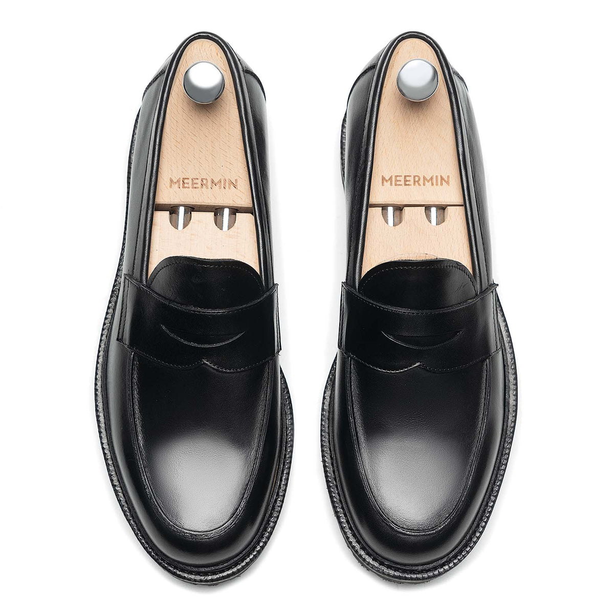 Top-down view of a pair of Meermin black boxcalf penny loafers on shoe trees, showing apron stitching and penny slot detail